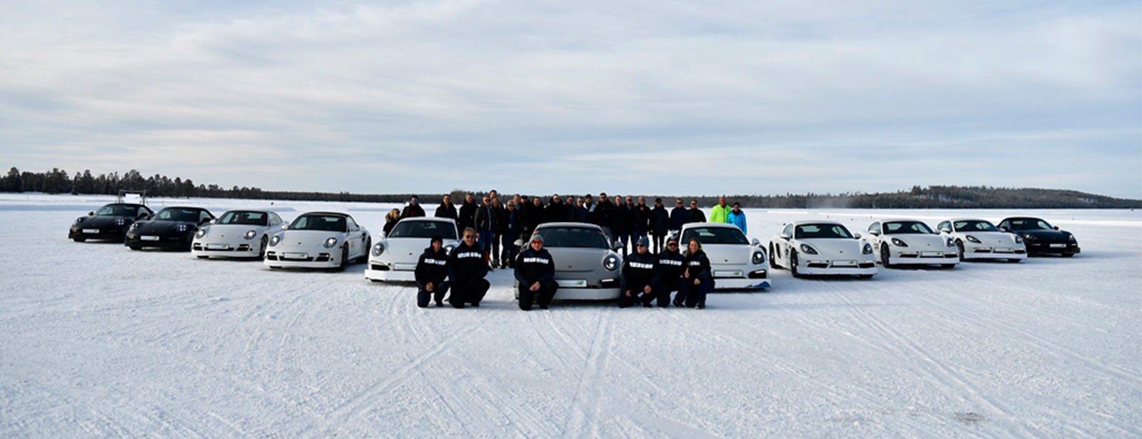 Porsche Fahrzeuge stehen aufgereiht auf dem Eis und Personen stehen herum.